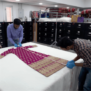 Eka_resources-STRATEGY_PLANNING Two people in blue gloves measuring an embroidered textile